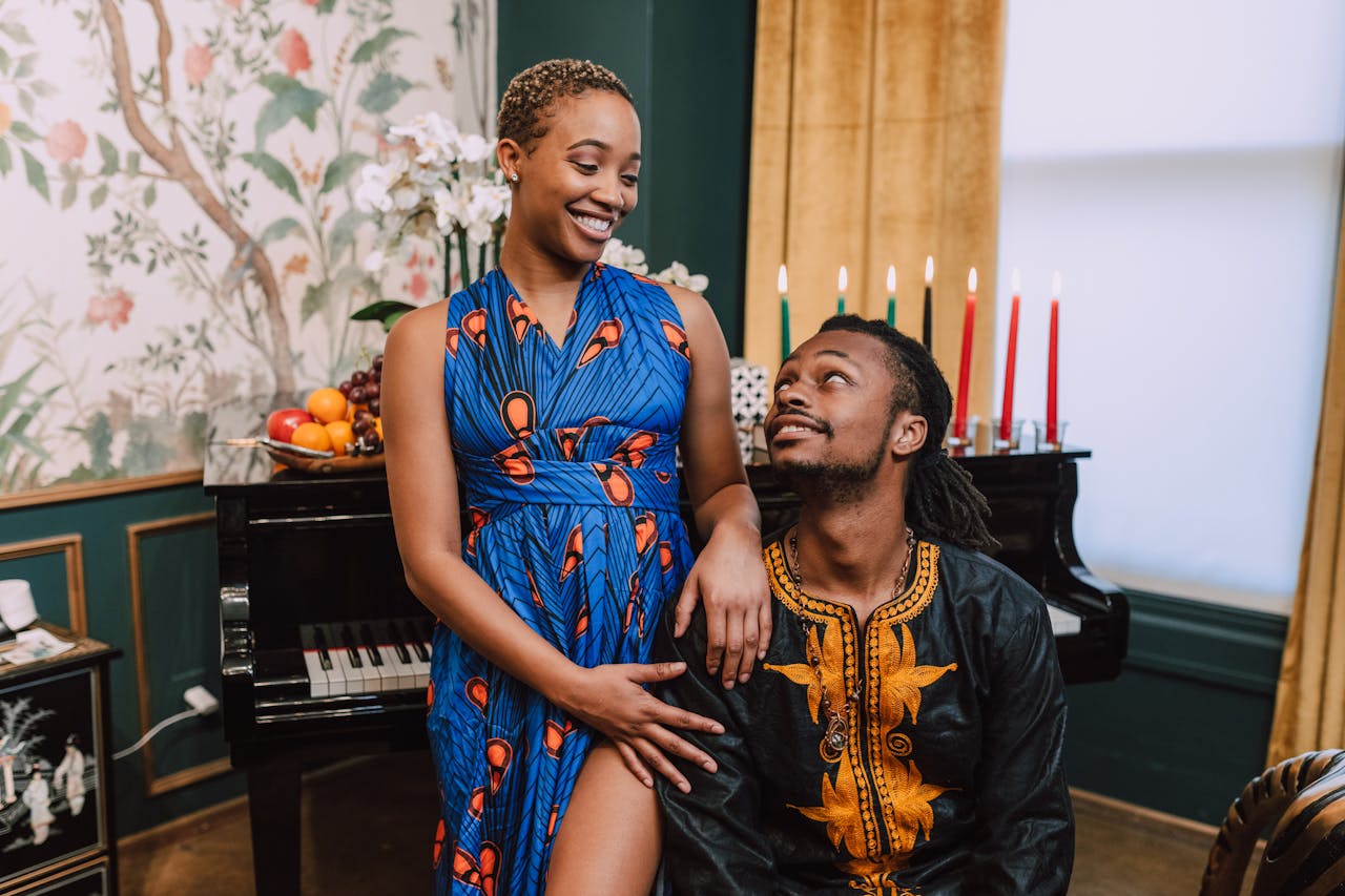 our-services-2 A happy couple celebrates Kwanzaa indoors, wearing colorful African traditional clothing beside a piano and Kinara.