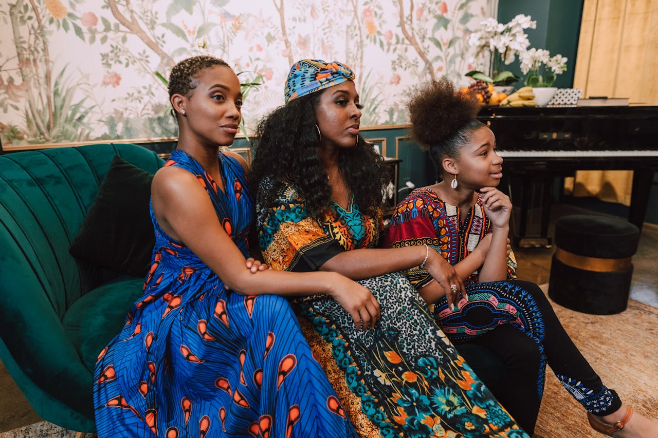 about-01 Three African women in colorful traditional clothing sitting indoors, exuding a sense of cultural pride.